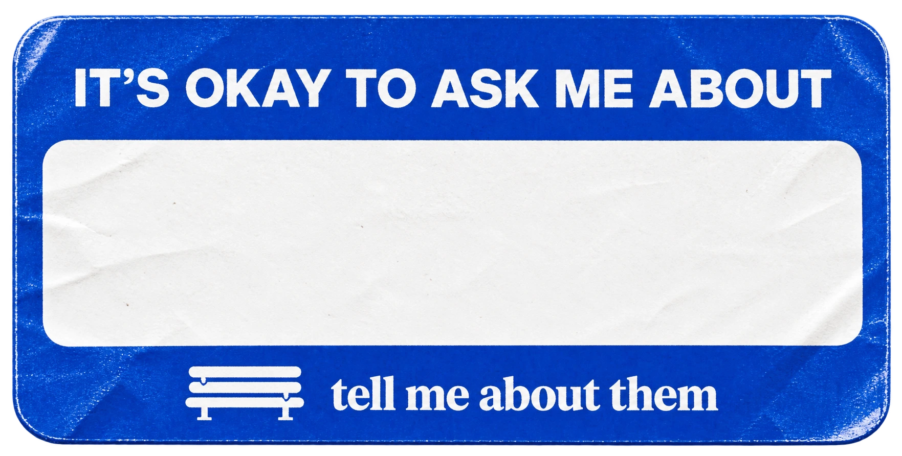 A worn blue badge reading It’s okay to ask me about, with a blank space for a name.